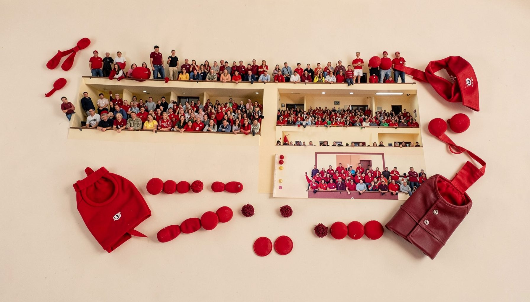A wide photograph of a packed gallery at a Rugby Fives tournament, with spectators lining the court balcony; warm cream walls and maroon accents in the crowd.